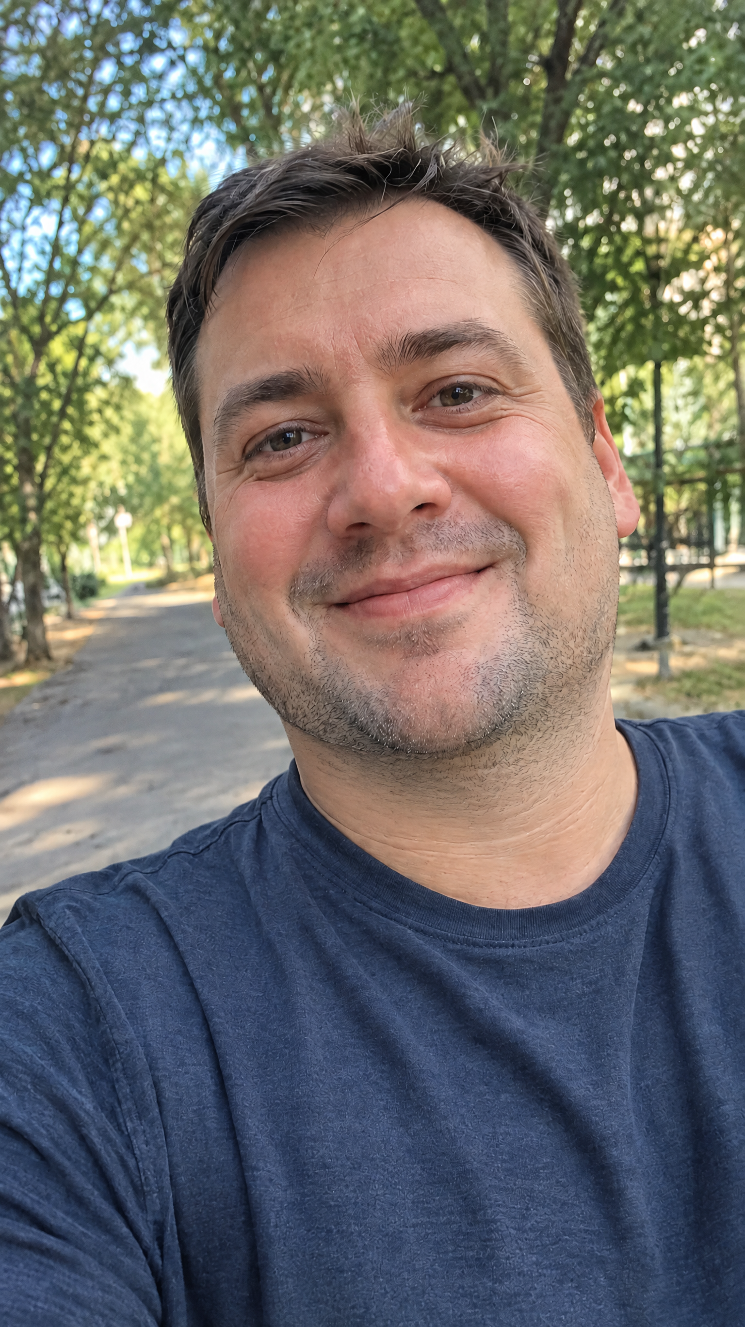The same outdoor selfie with the double chin reduced and the jawline naturally contoured, preserving his smile and skin details.
