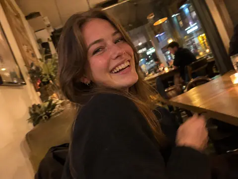Candid smartphone snapshot of a laughing young woman in a dimly lit, cozy restaurant with slight camera tilt and subtle motion blur.